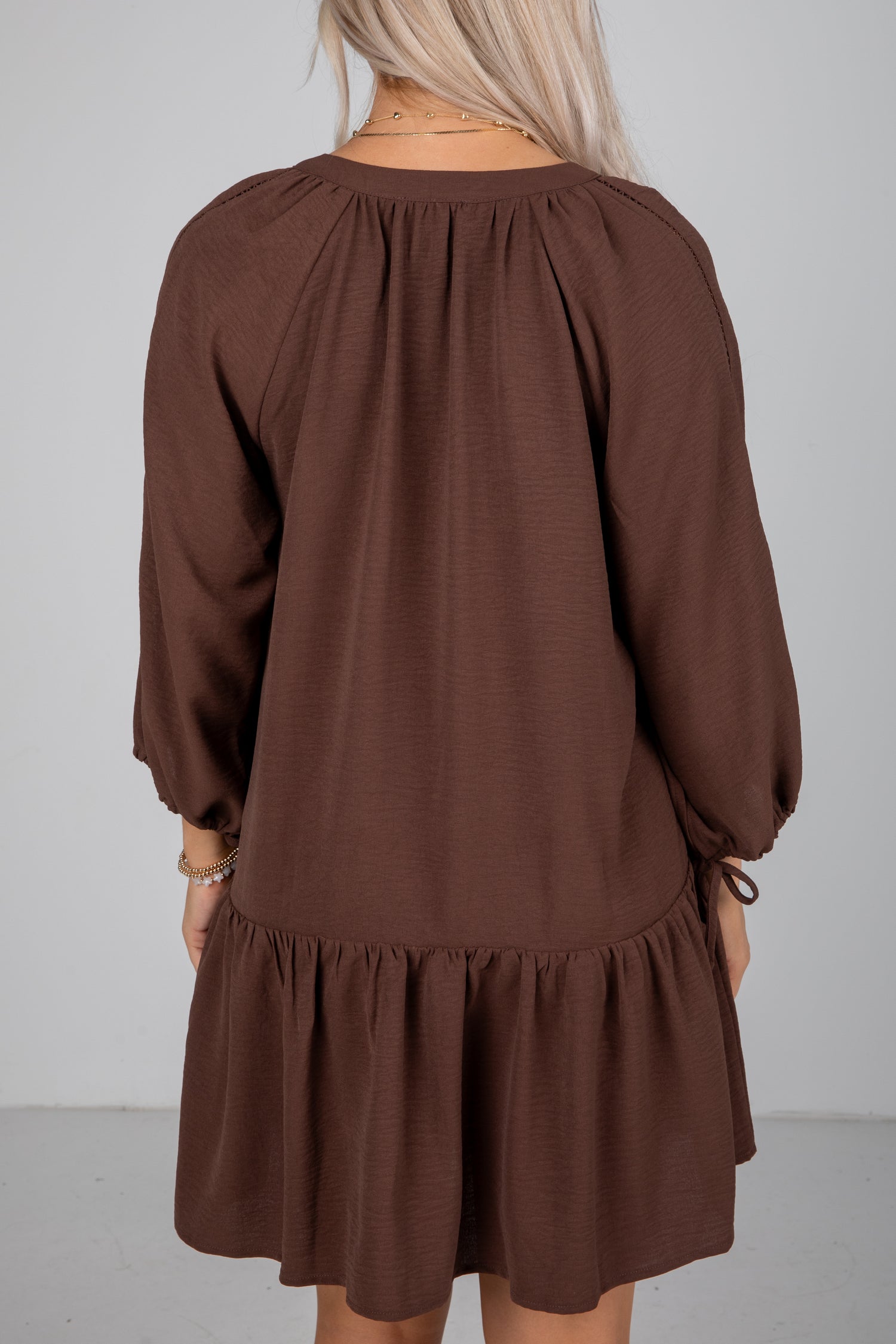 Brown dress with long sleeves and a ruffled skirt on a plain background