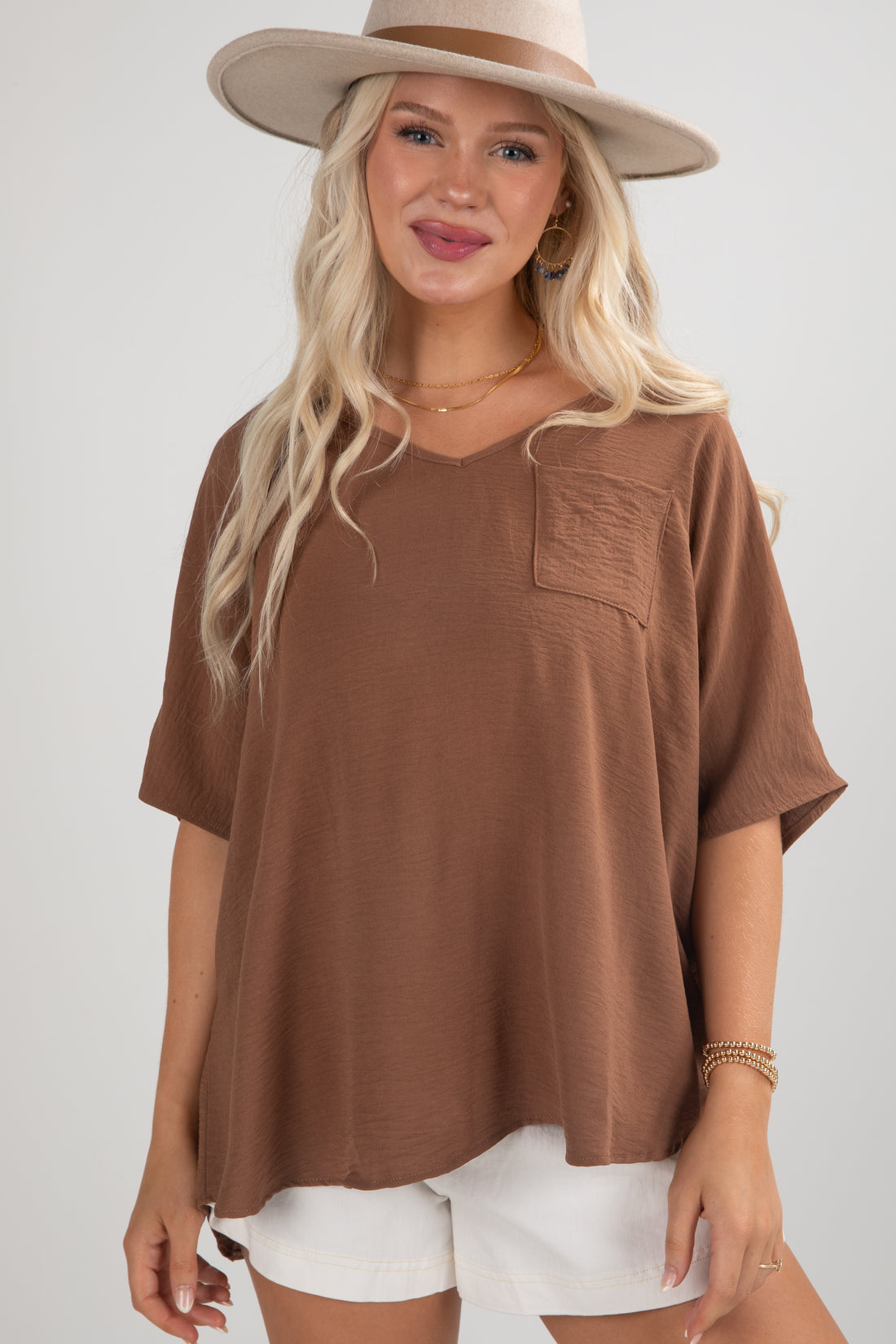 Woman wearing a brown oversized t-shirt and white shorts with a beige hat on a plain background