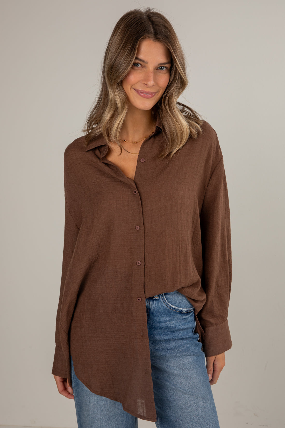 Woman wearing a brown button-up shirt and blue jeans against a plain background