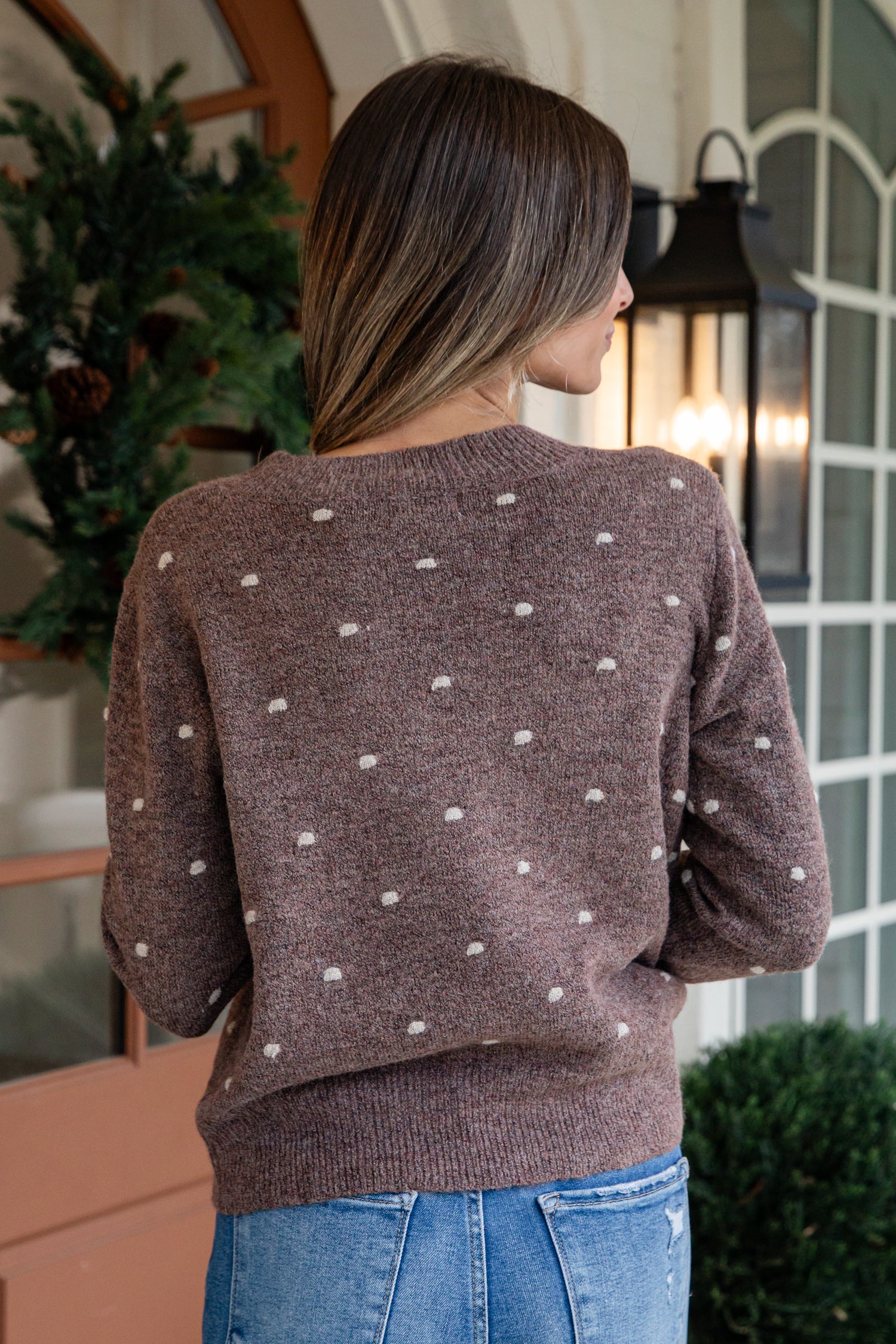 Woman wearing a brown sweater with white polka dots in an indoor setting.