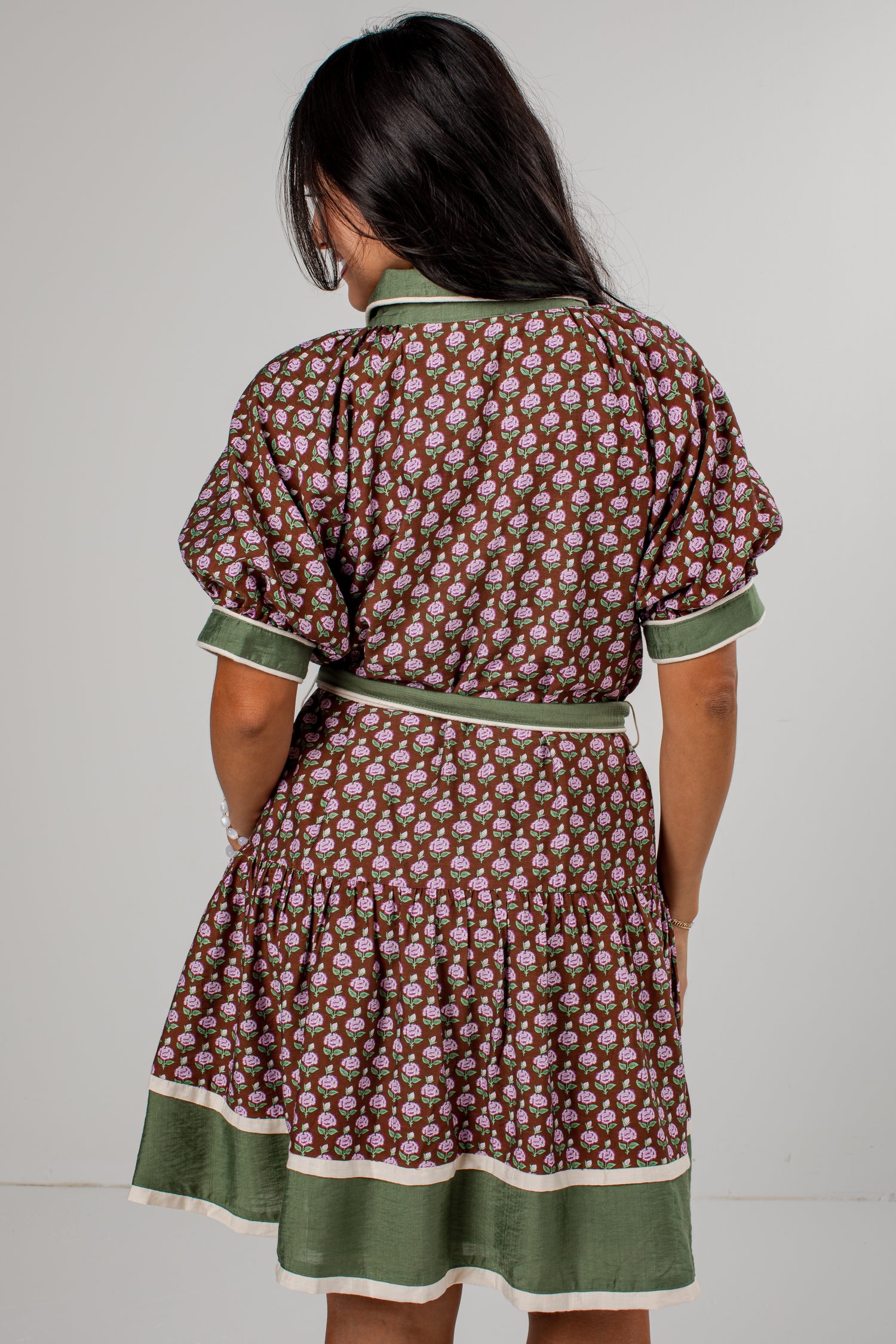A woman viewed from the back wearing a brown and green patterned dress with a matching belt and green trim.
