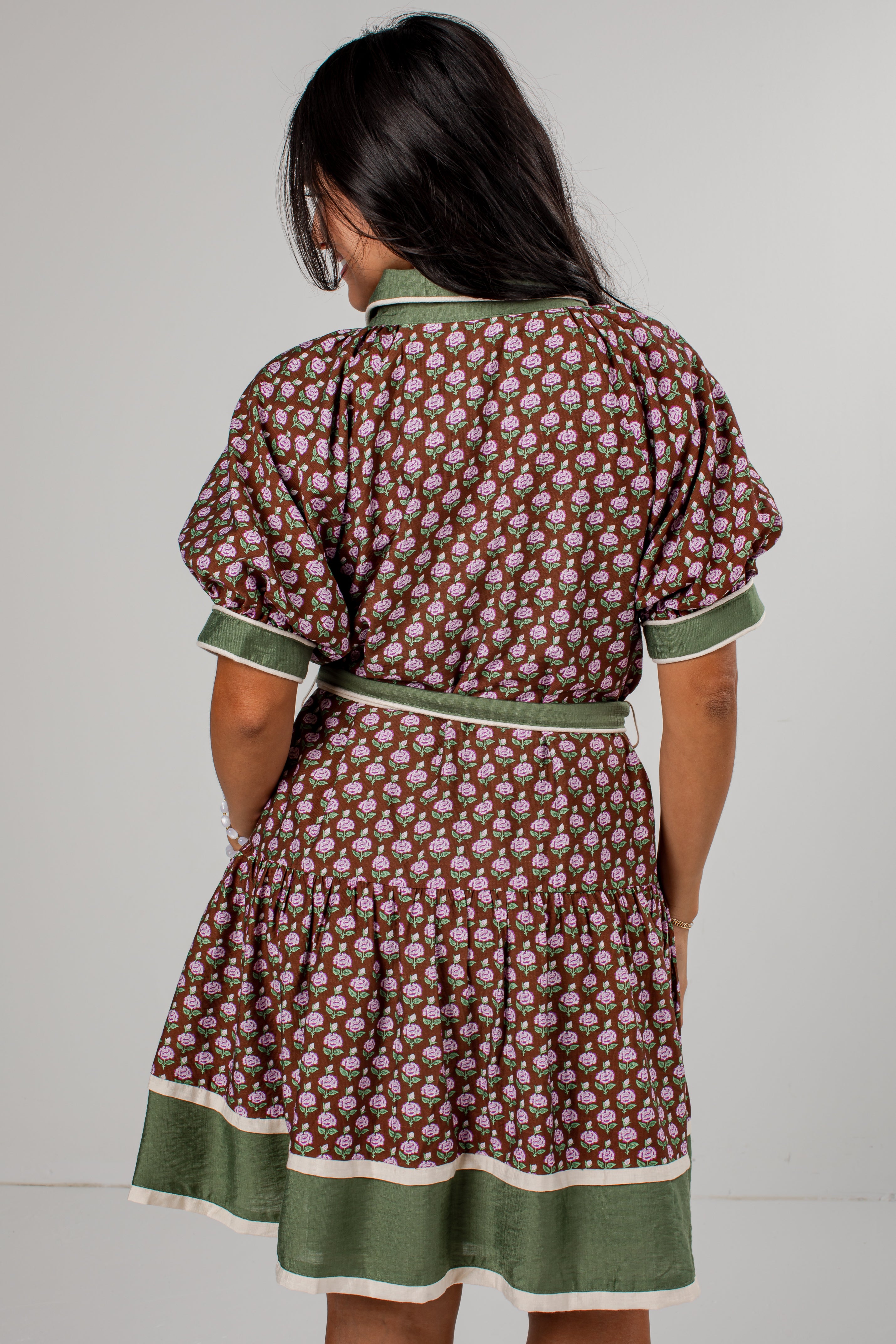 A woman viewed from the back wearing a brown and green patterned dress with a matching belt and green trim.