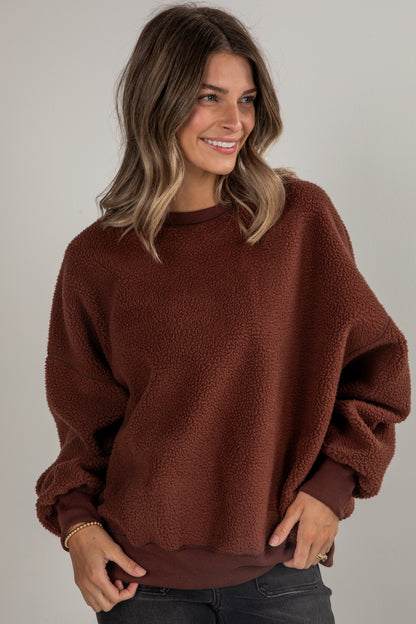 Woman wearing a brown sweater against a plain background