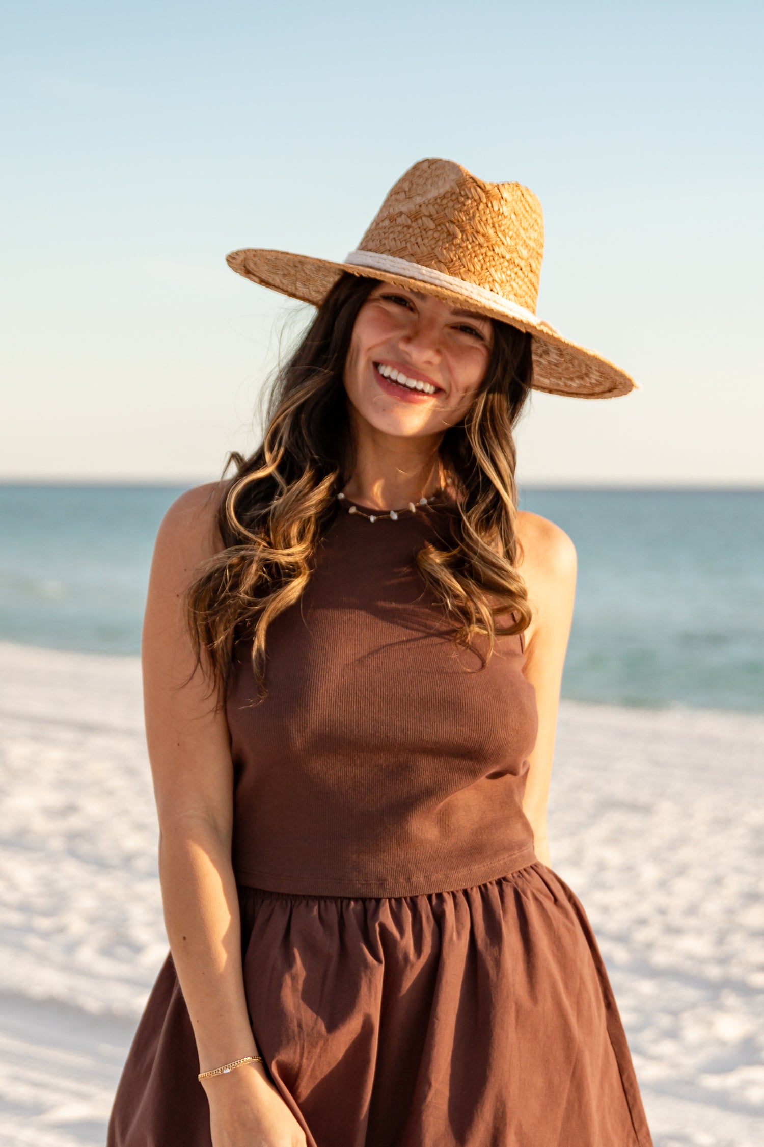 Woman wearing a brown dress and straw hat on a beach