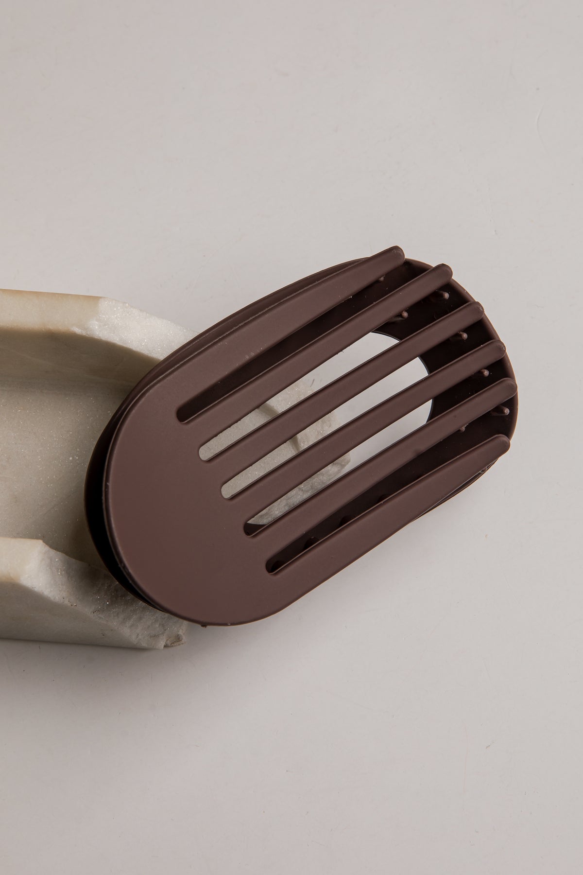 A dark brown silicone spatula with a slotted design, shown resting on a light gray background.
