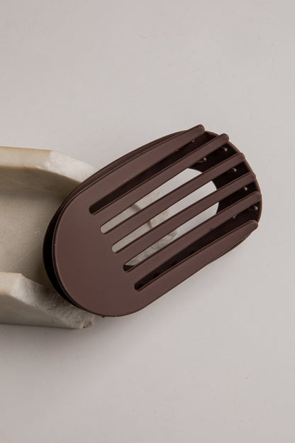 A dark brown silicone spatula with a slotted design, shown resting on a light gray background.