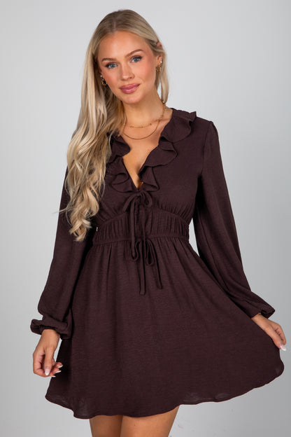 Woman wearing a brown dress with long sleeves on a gray background