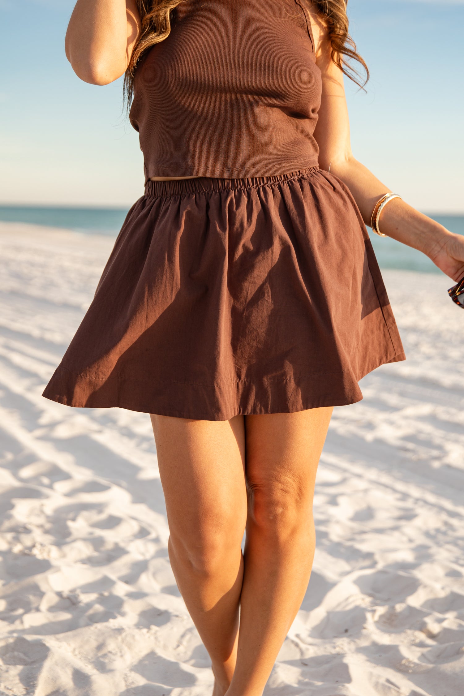 Woman in a brown dress standing on a sandy beach with ocean view