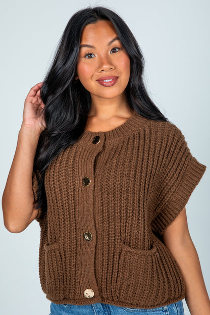 Woman wearing a brown knitted vest against a plain background