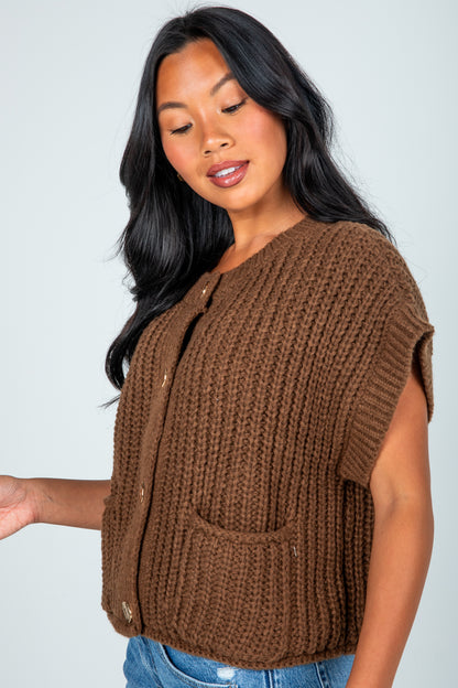 Woman wearing a brown knitted vest against a plain background