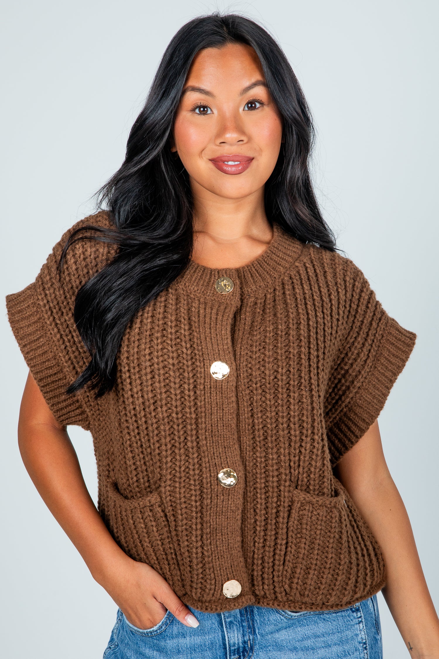 Woman wearing a brown knitted vest with button details against a plain background