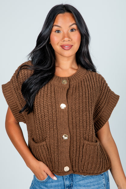 Woman wearing a brown knitted vest with button details against a plain background
