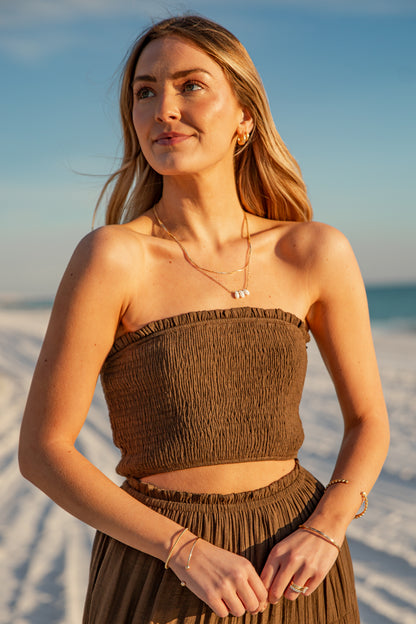 Woman in a brown strapless top and skirt standing on a beach with a clear sky.