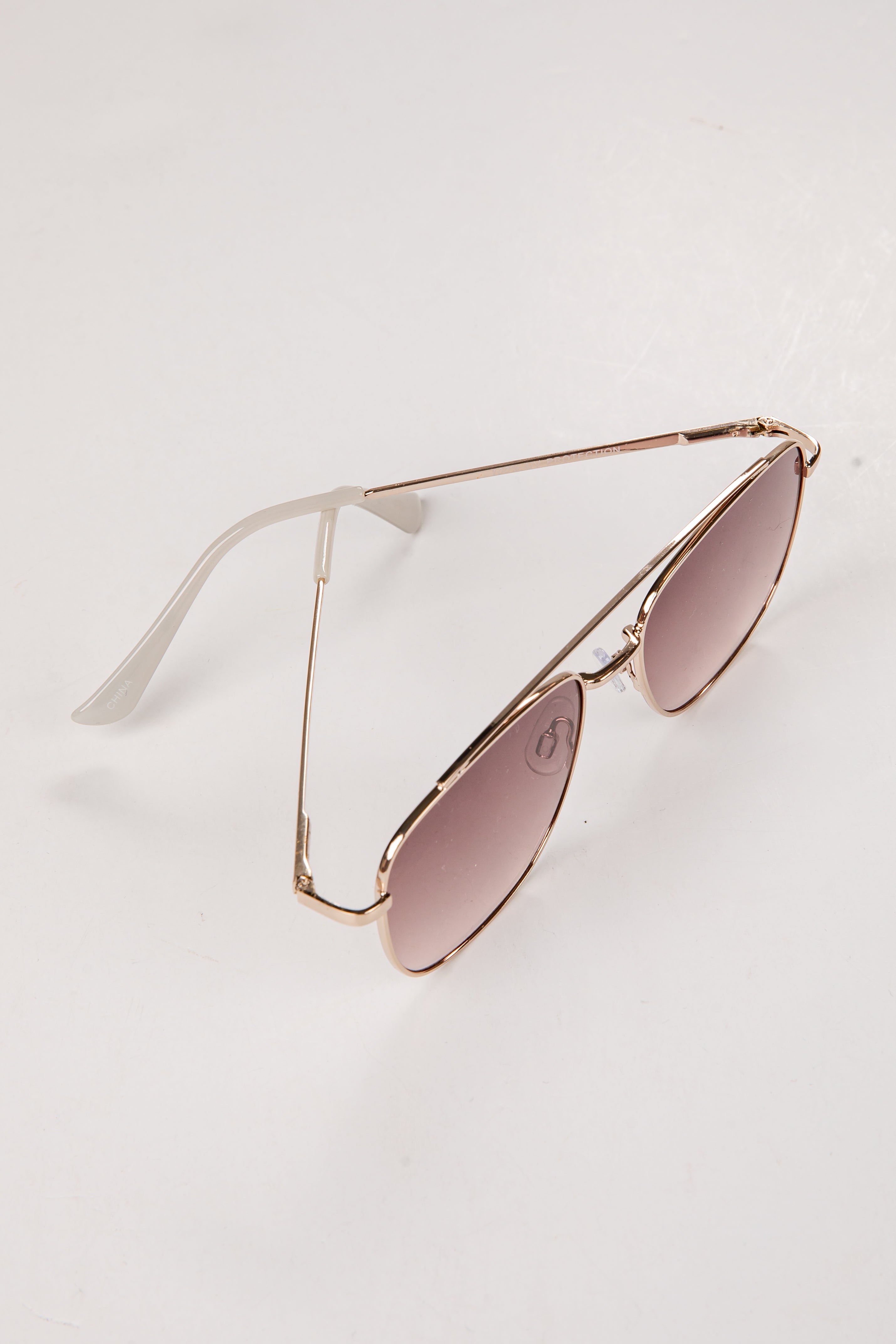 Sunglasses with gold frame and pink lenses on a light gray background