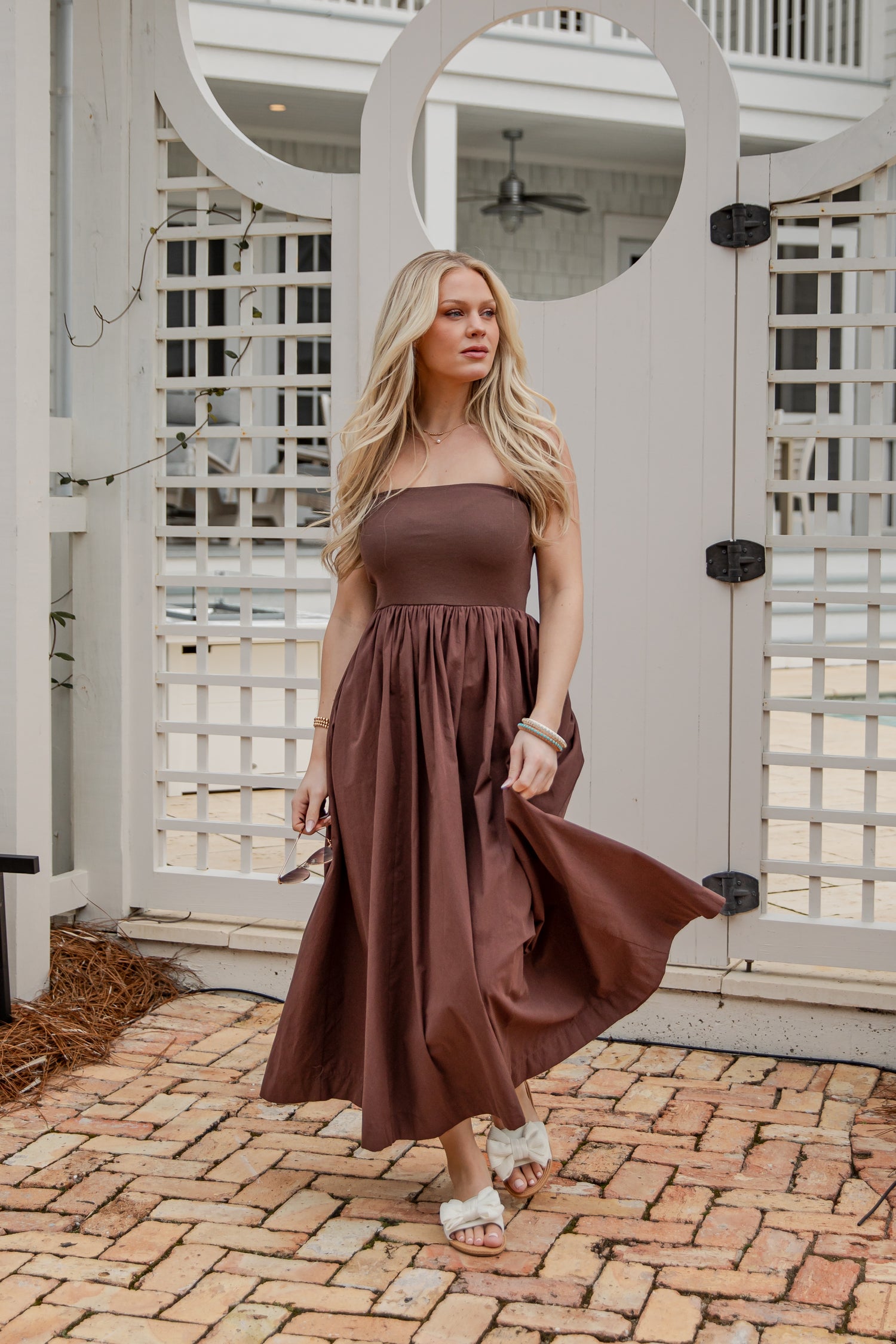 Woman in a brown dress standing on a brick patio with a white lattice background