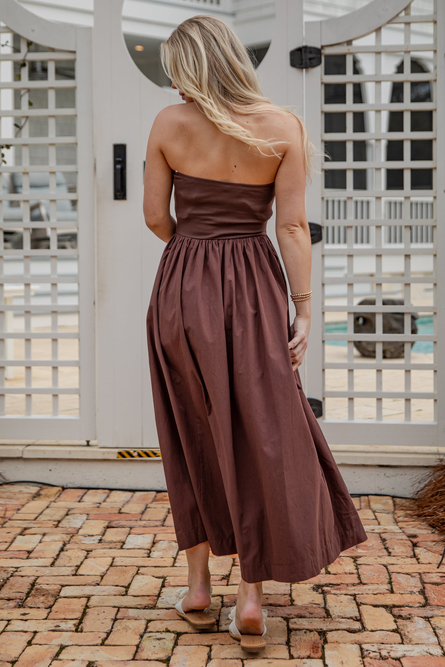 Woman wearing a brown strapless dress standing on a brick patio.