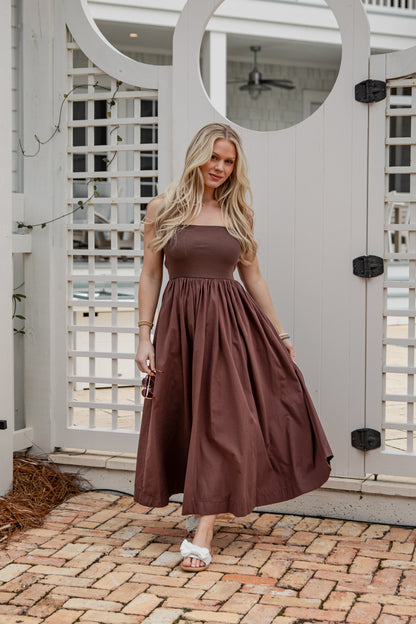 Woman in a brown dress standing in front of a white lattice door.