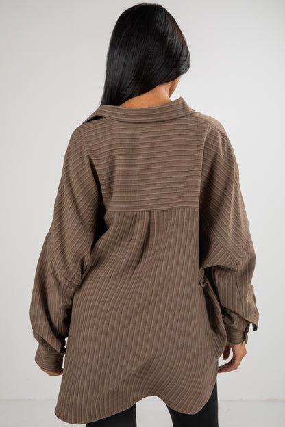 Person wearing a brown ribbed sweater against a white background