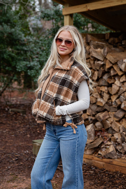 Woman wearing a plaid vest and sunglasses standing in front of stacked firewood.