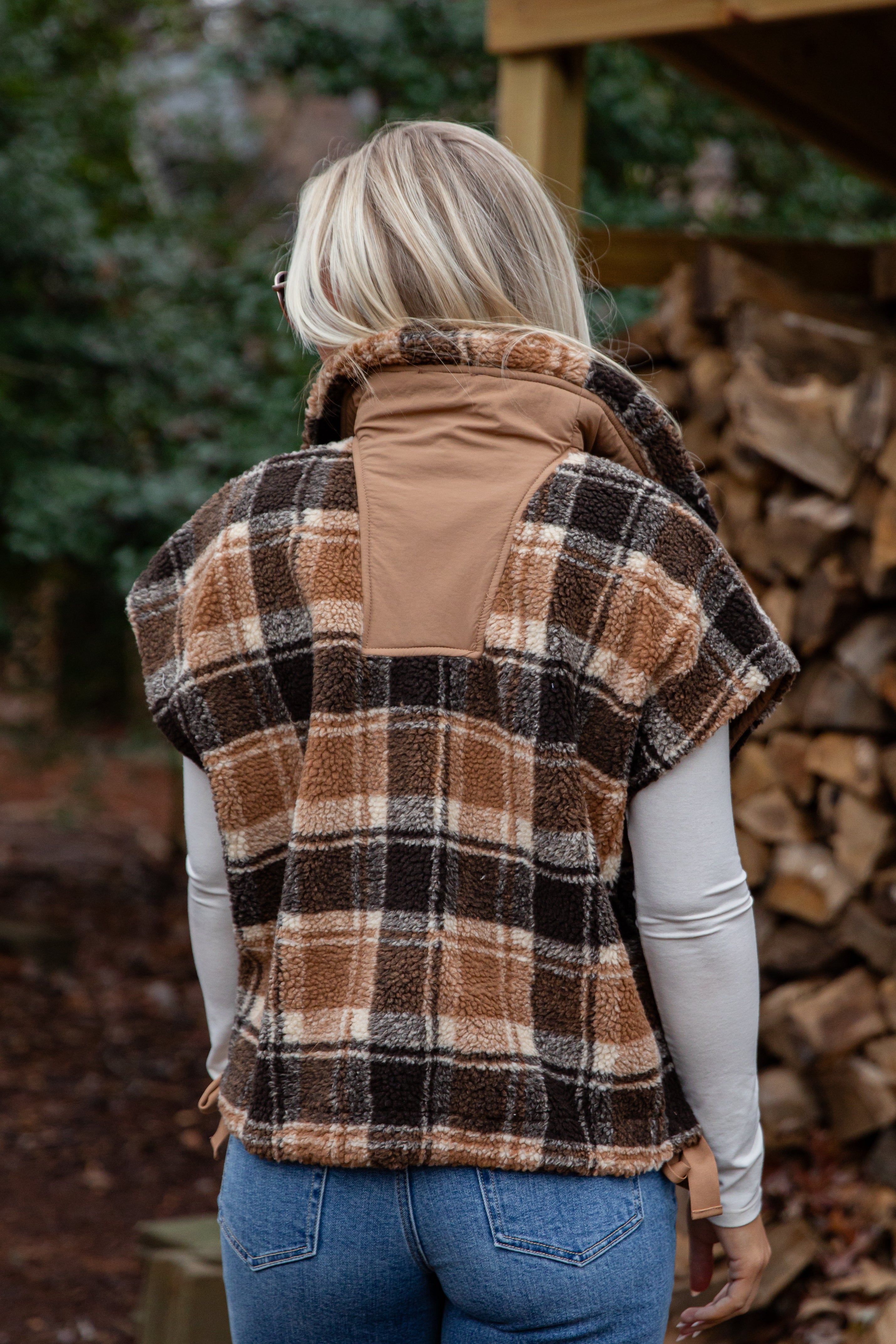 Person wearing a plaid vest over a beige jacket in a forest setting