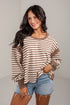 A woman modeling a brown and beige horizontally striped long-sleeve top with solid brown trim, paired with denim shorts, against a light gray studio background.