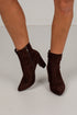 A pair of dark brown suede ankle boots with pointed toes and block heels, shown on a model&