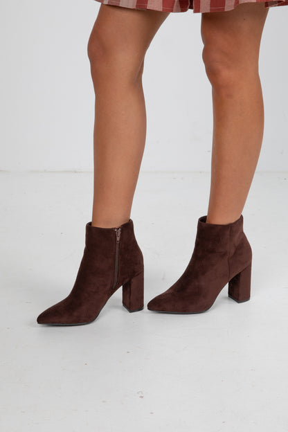 Brown suede ankle boots worn with a plaid skirt on a white background