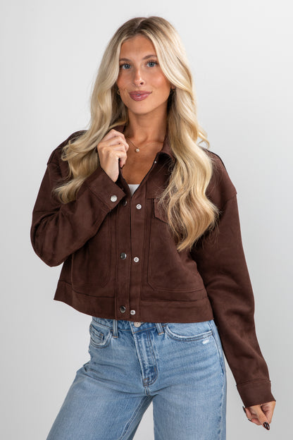 Woman wearing a brown jacket and blue jeans against a plain background