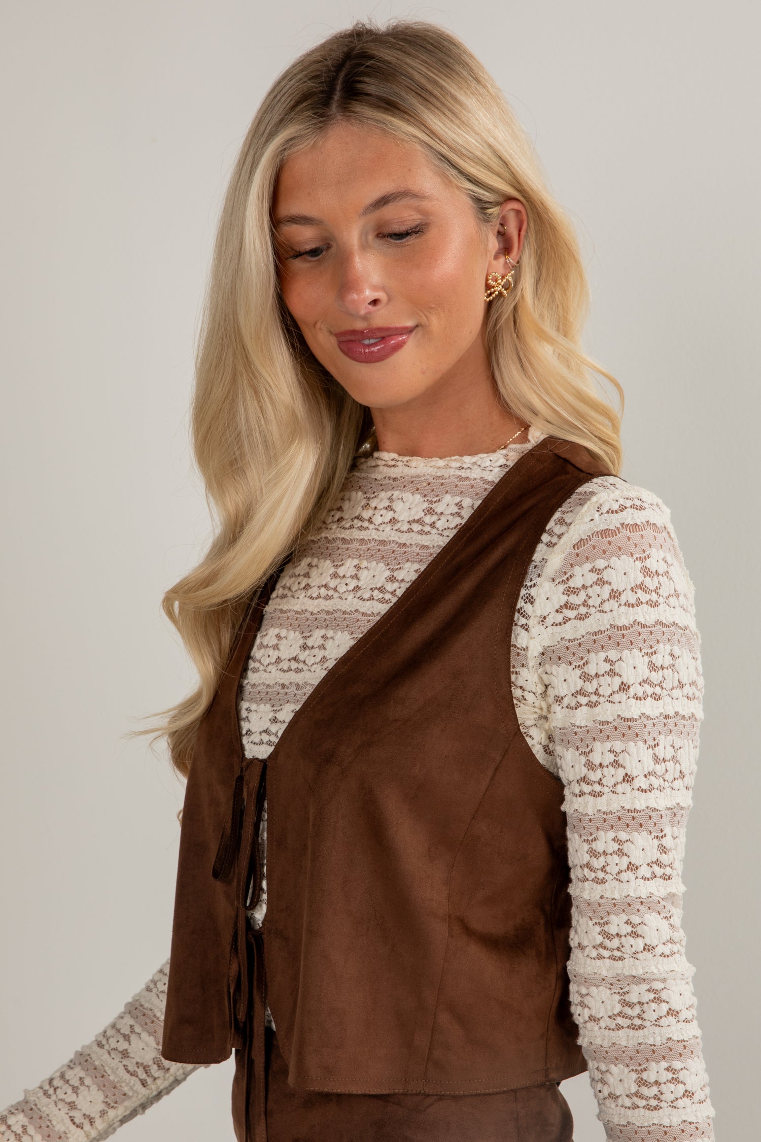 Woman wearing a brown vest over a patterned top against a plain background