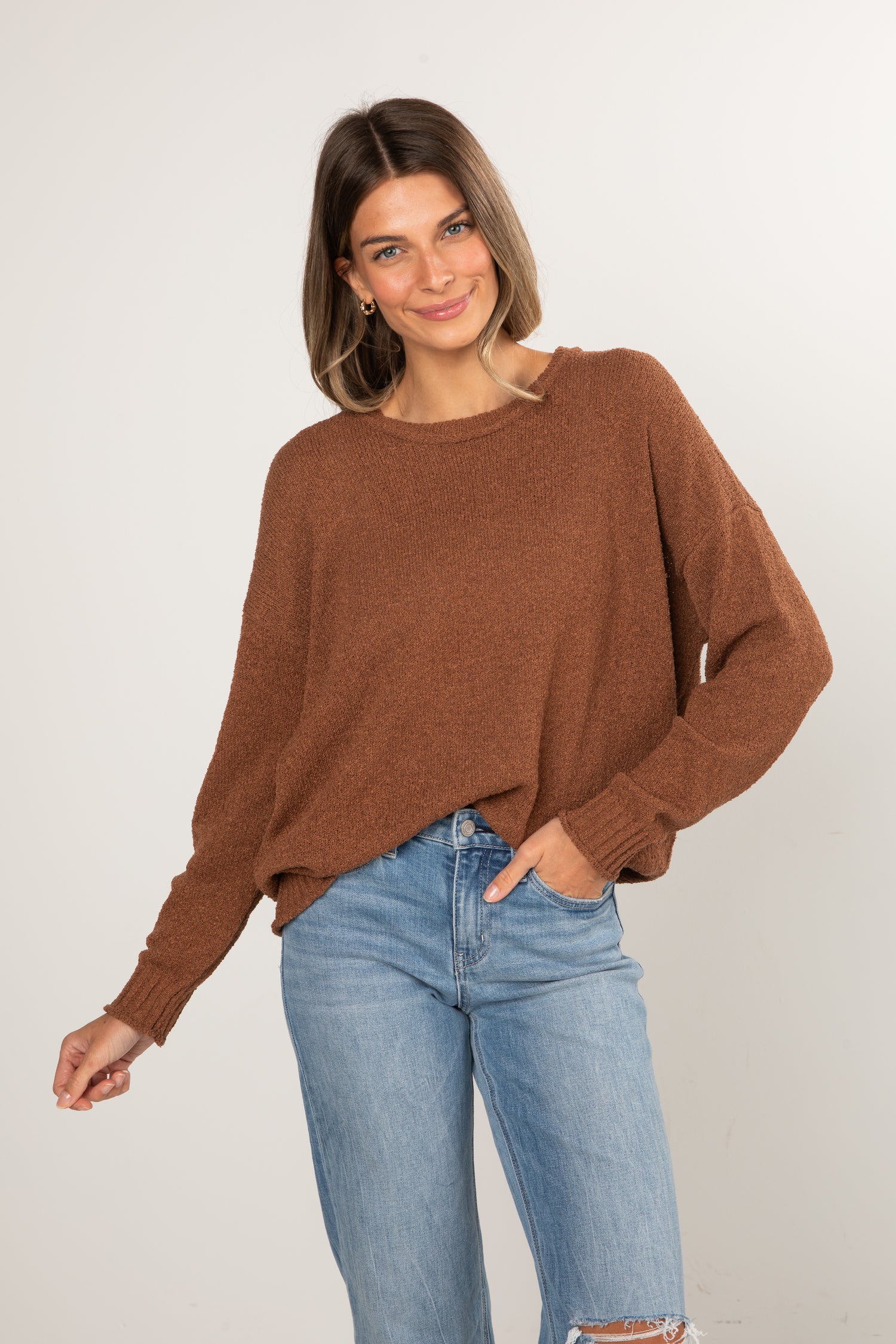 Woman wearing a brown sweater and blue jeans against a white background