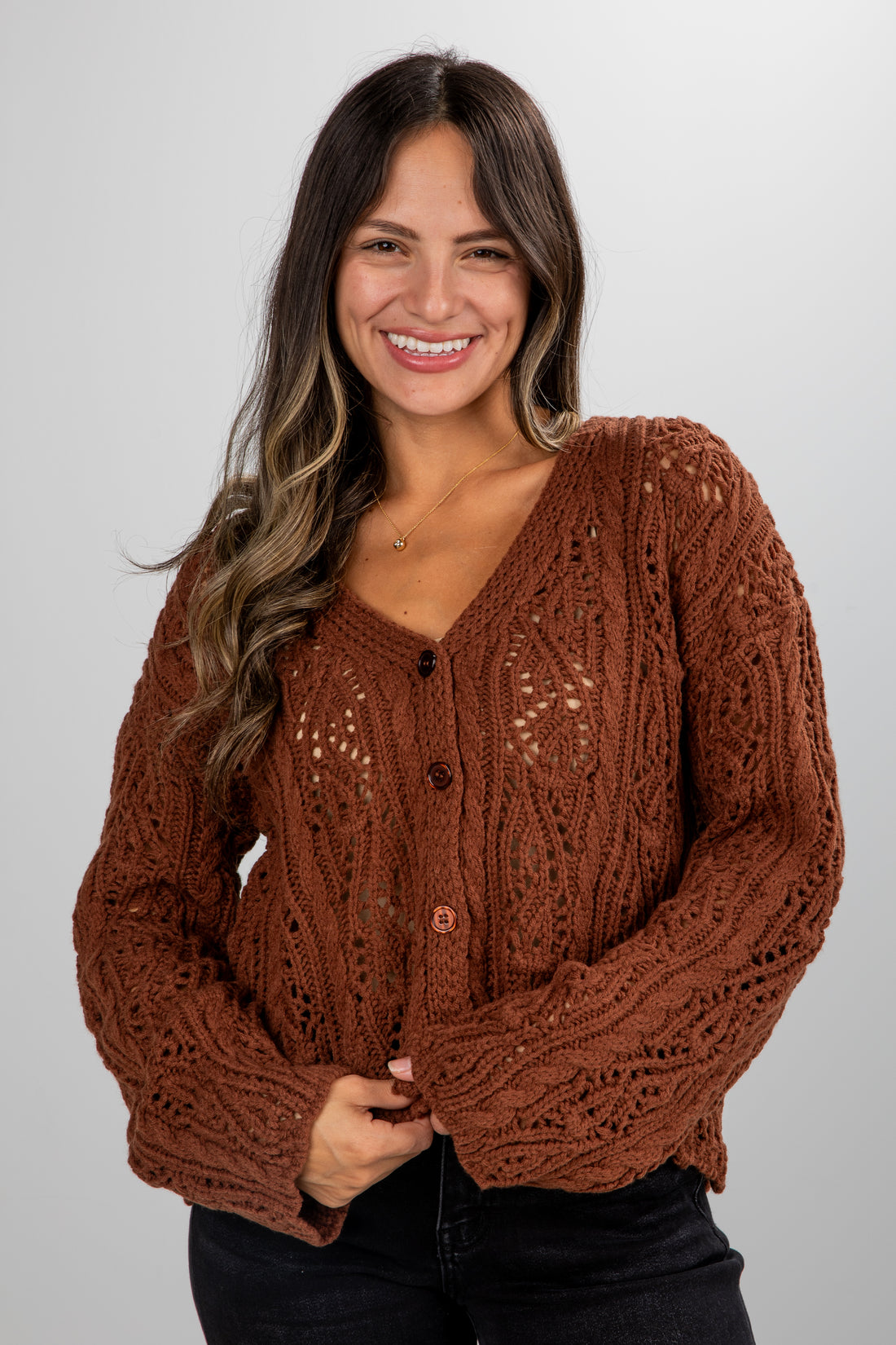 Woman wearing a brown cable knit cardigan against a plain background