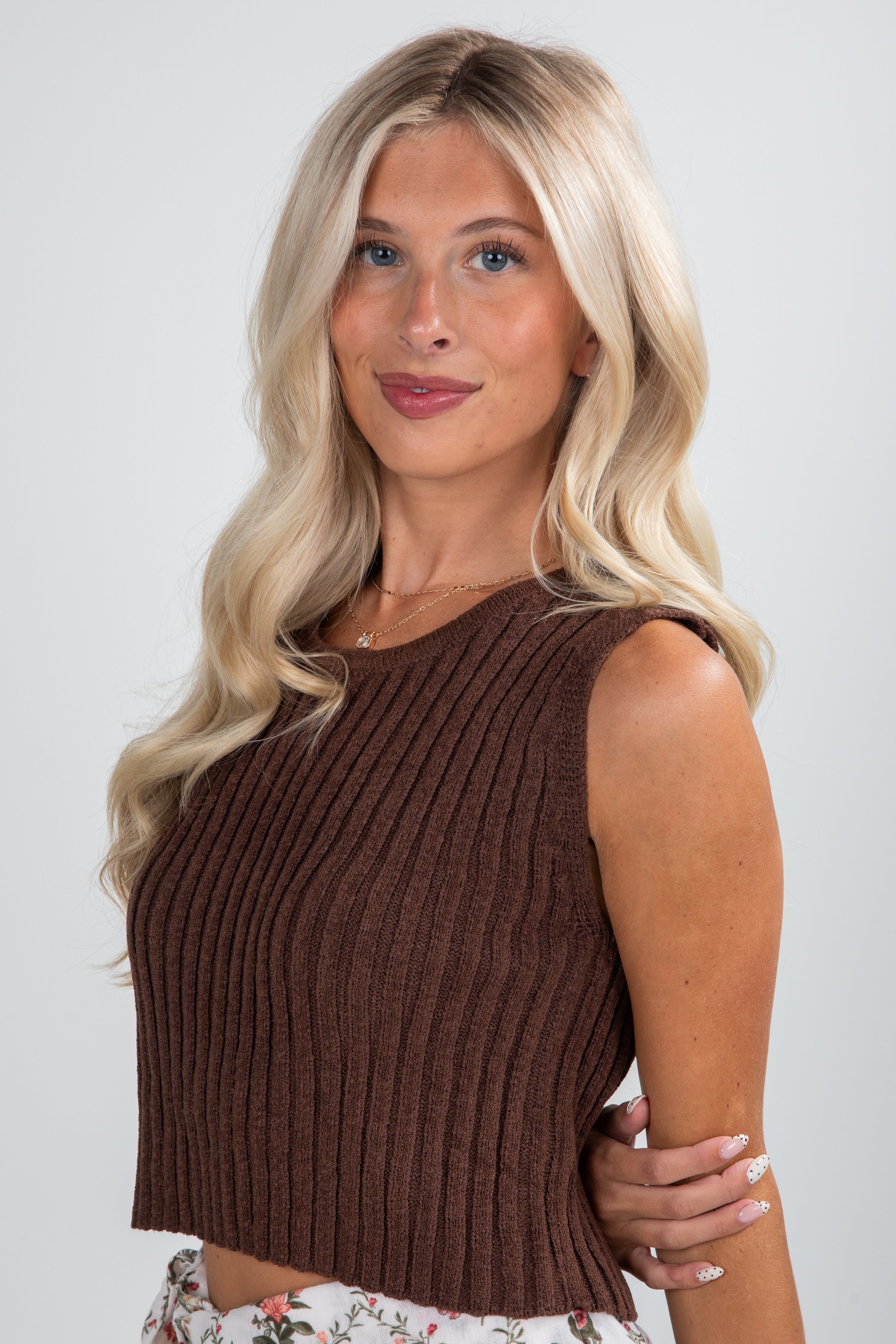 Woman wearing a brown ribbed tank top against a plain background