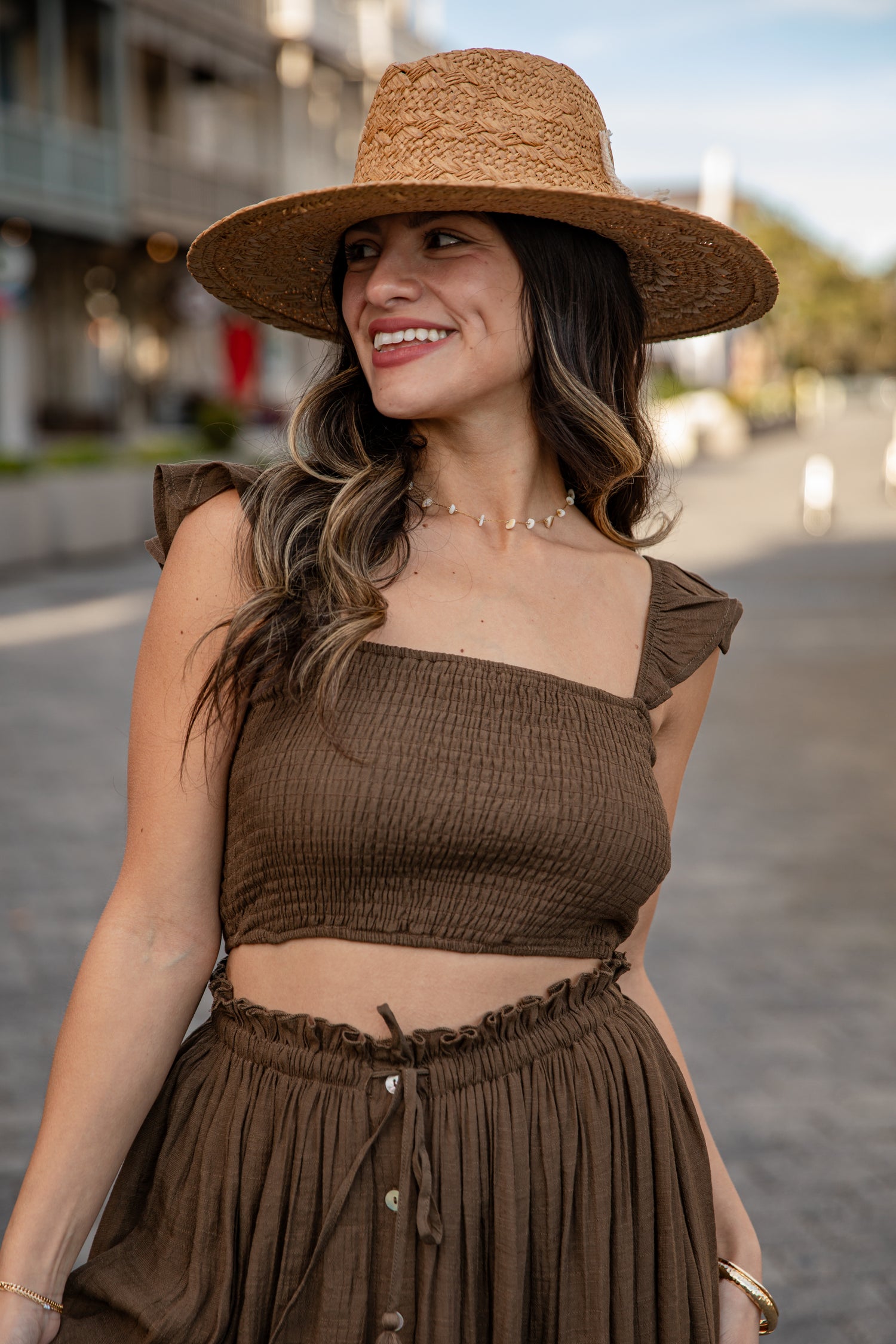 Woman wearing a brown outfit with a straw hat on a street.