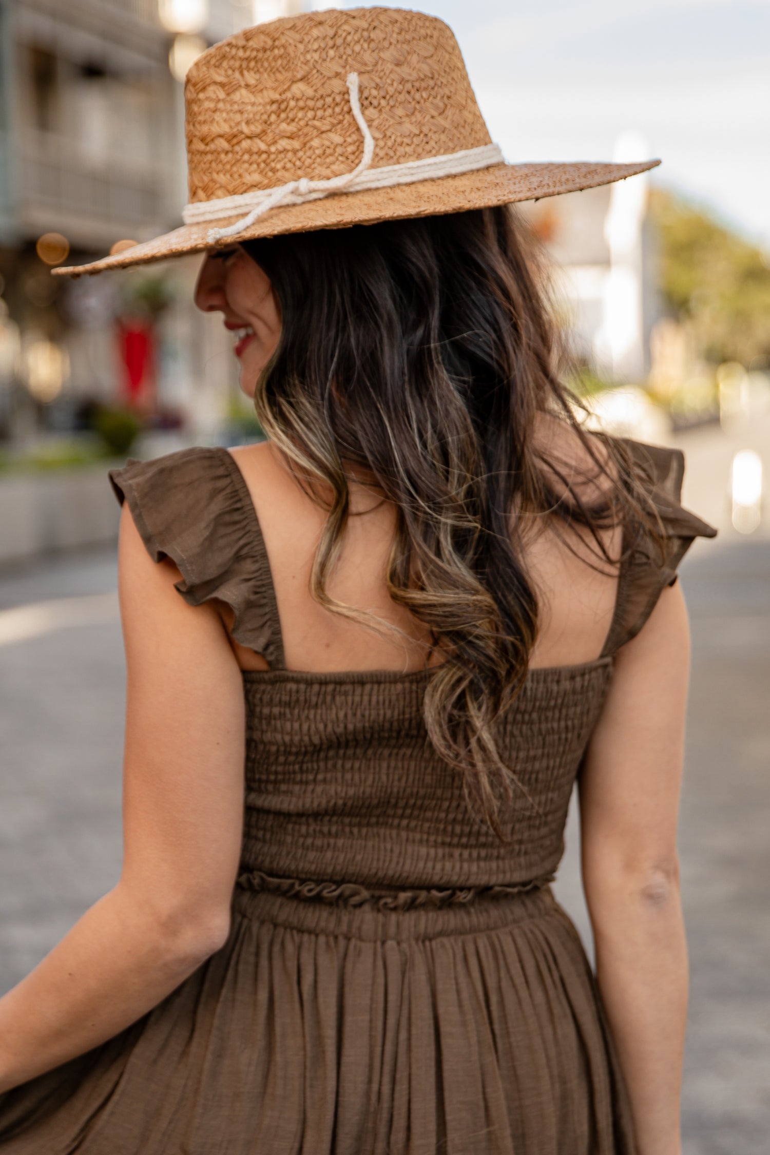 Woman wearing a brown dress and straw hat in an outdoor setting
