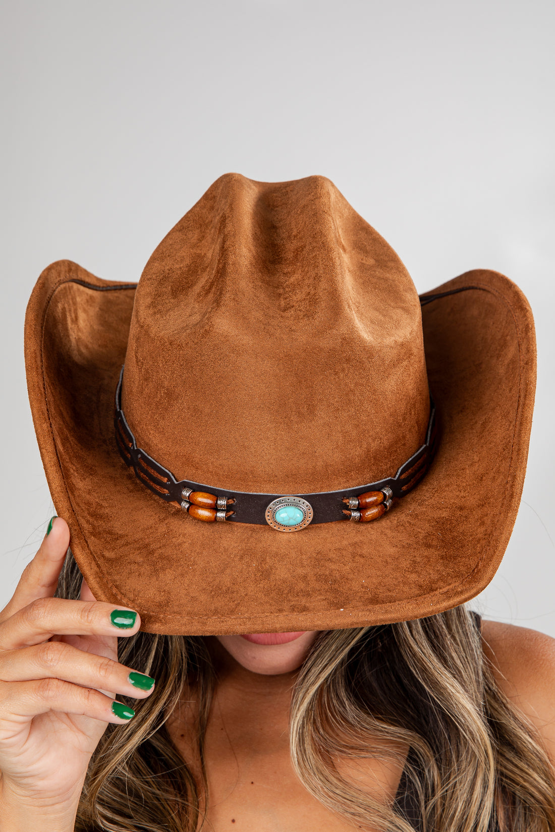 Brown cowboy hat with a decorative band held by a person against a neutral background