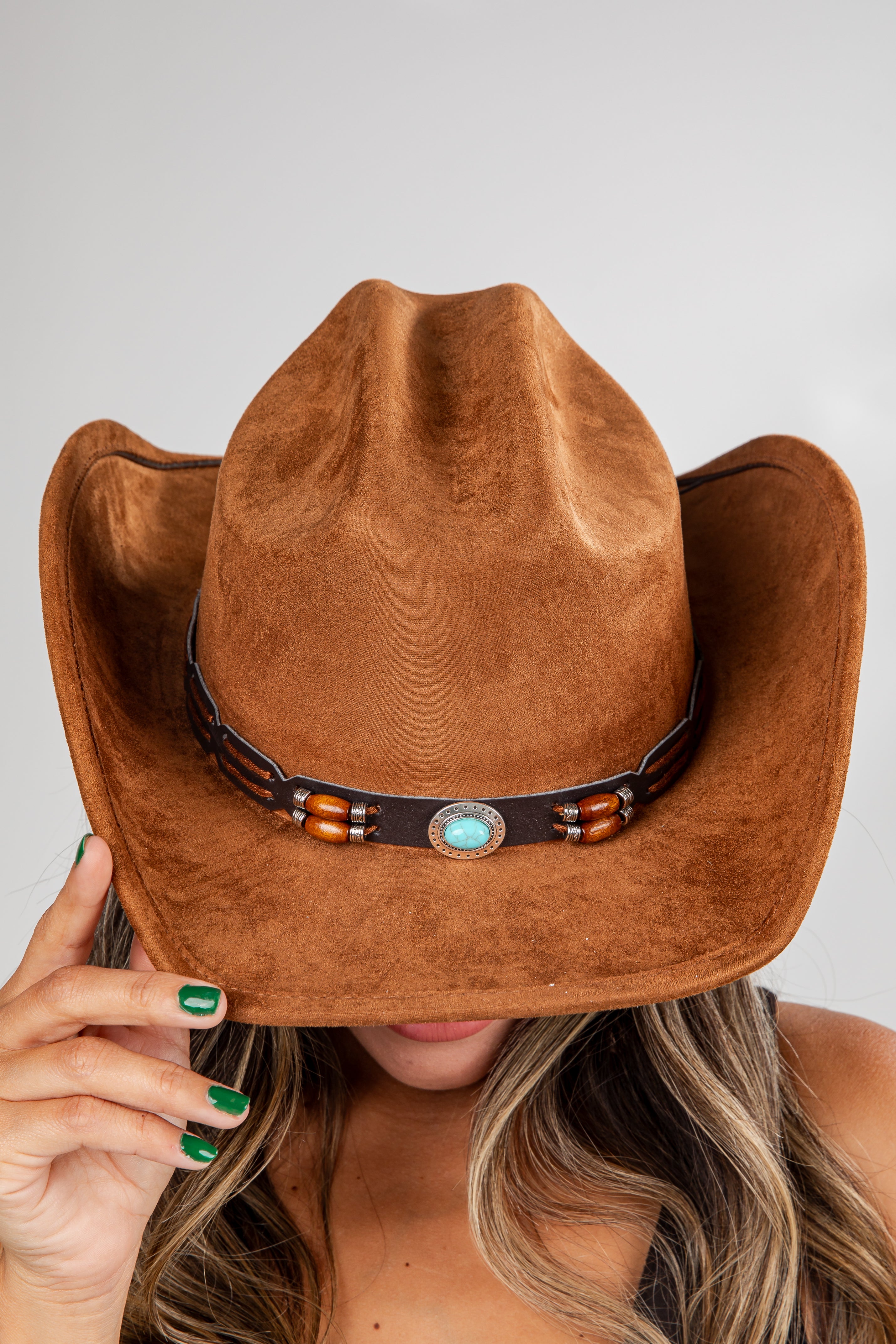 Brown cowboy hat with a decorative band held by a person against a neutral background