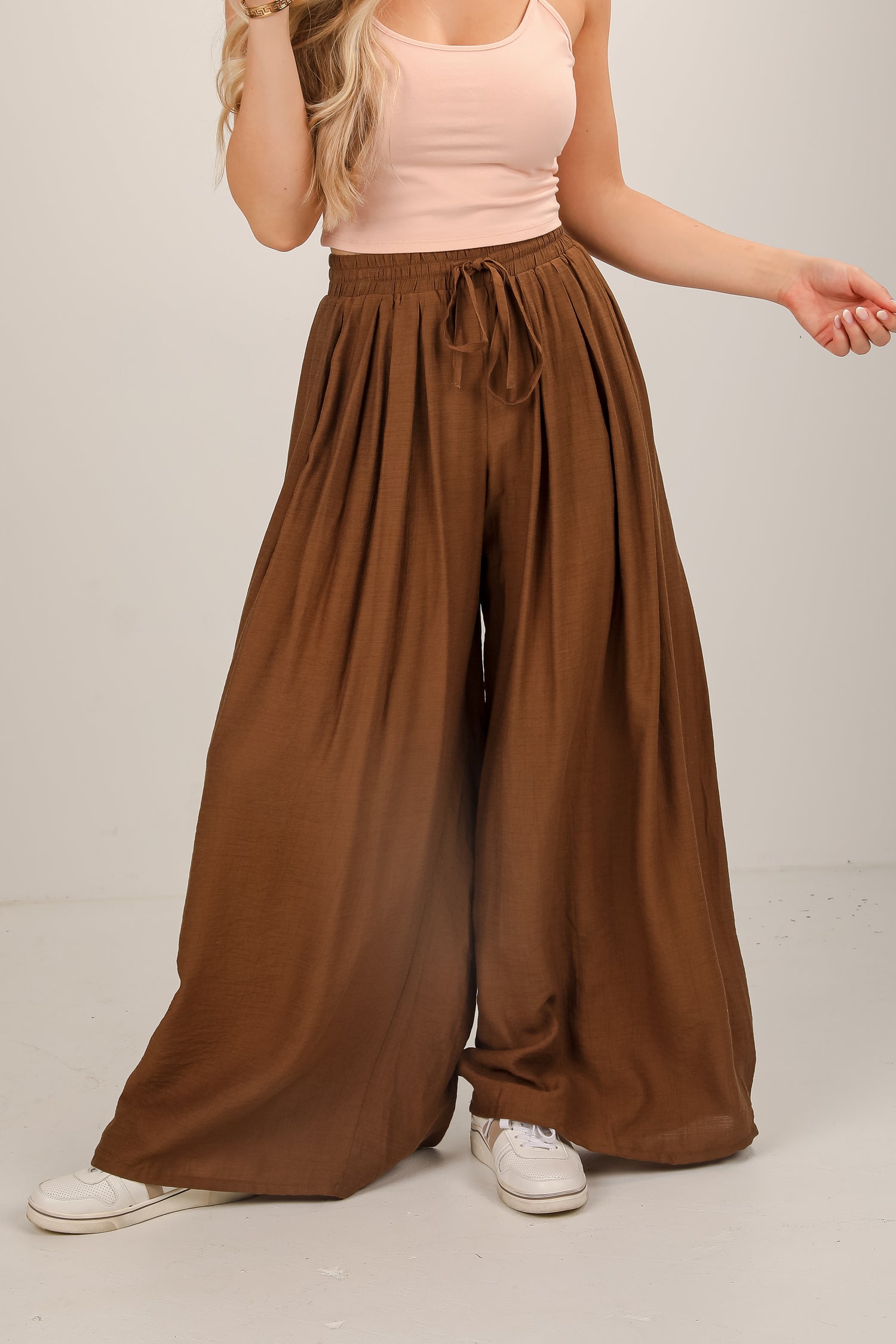 Person wearing brown wide-leg pants and a light pink top on a plain background