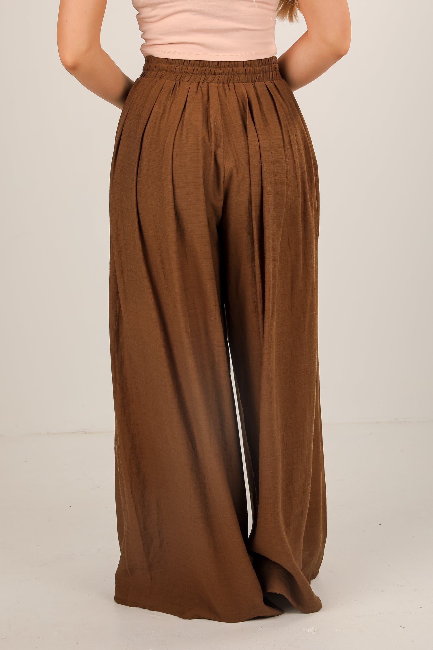 Brown wide-leg pants worn by a person on a beige background