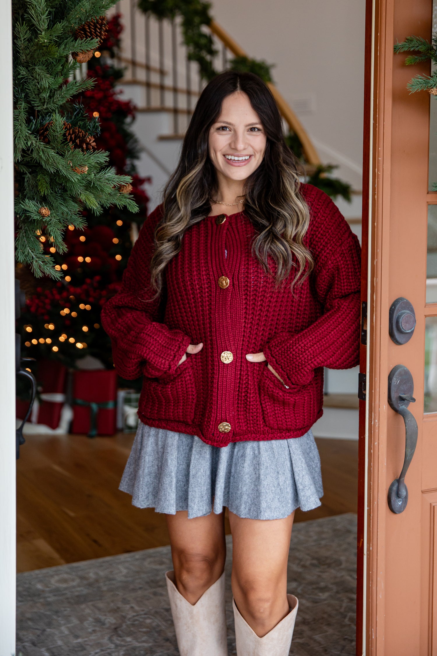 Woman wearing a red sweater and gray skirt standing in a home setting with a Christmas tree.