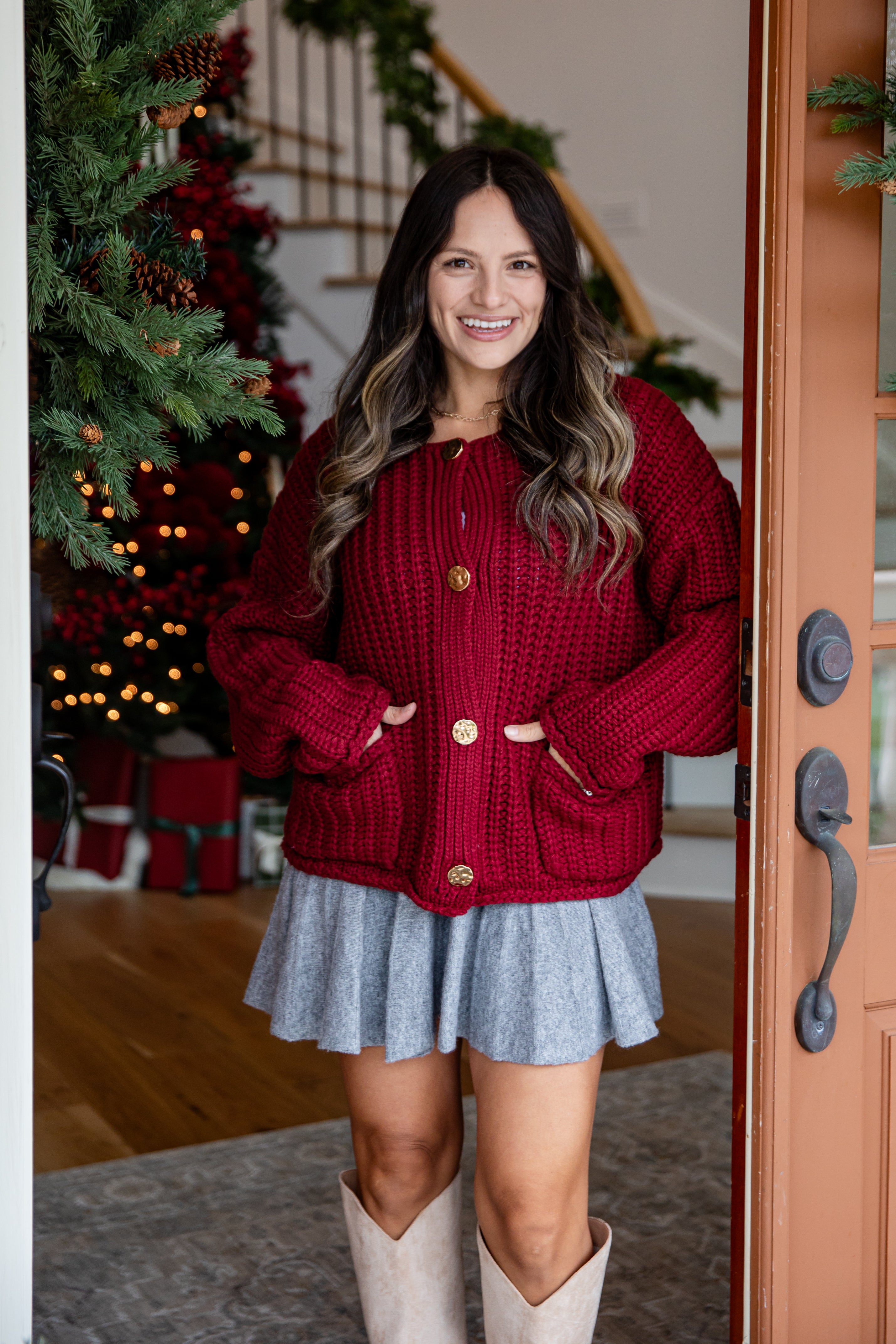 Woman wearing a red sweater and gray skirt standing in a home setting with a Christmas tree.