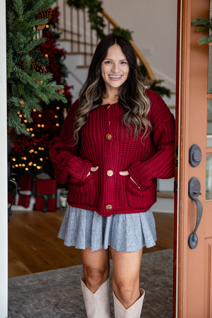 Woman wearing a red sweater and gray skirt standing in a home setting with a Christmas tree.