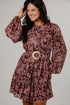 A woman modeling a long-sleeve mini dress with a brown and burgundy abstract pattern, featuring a matching waist belt with a light wood-look buckle, set against a plain light gray studio background.