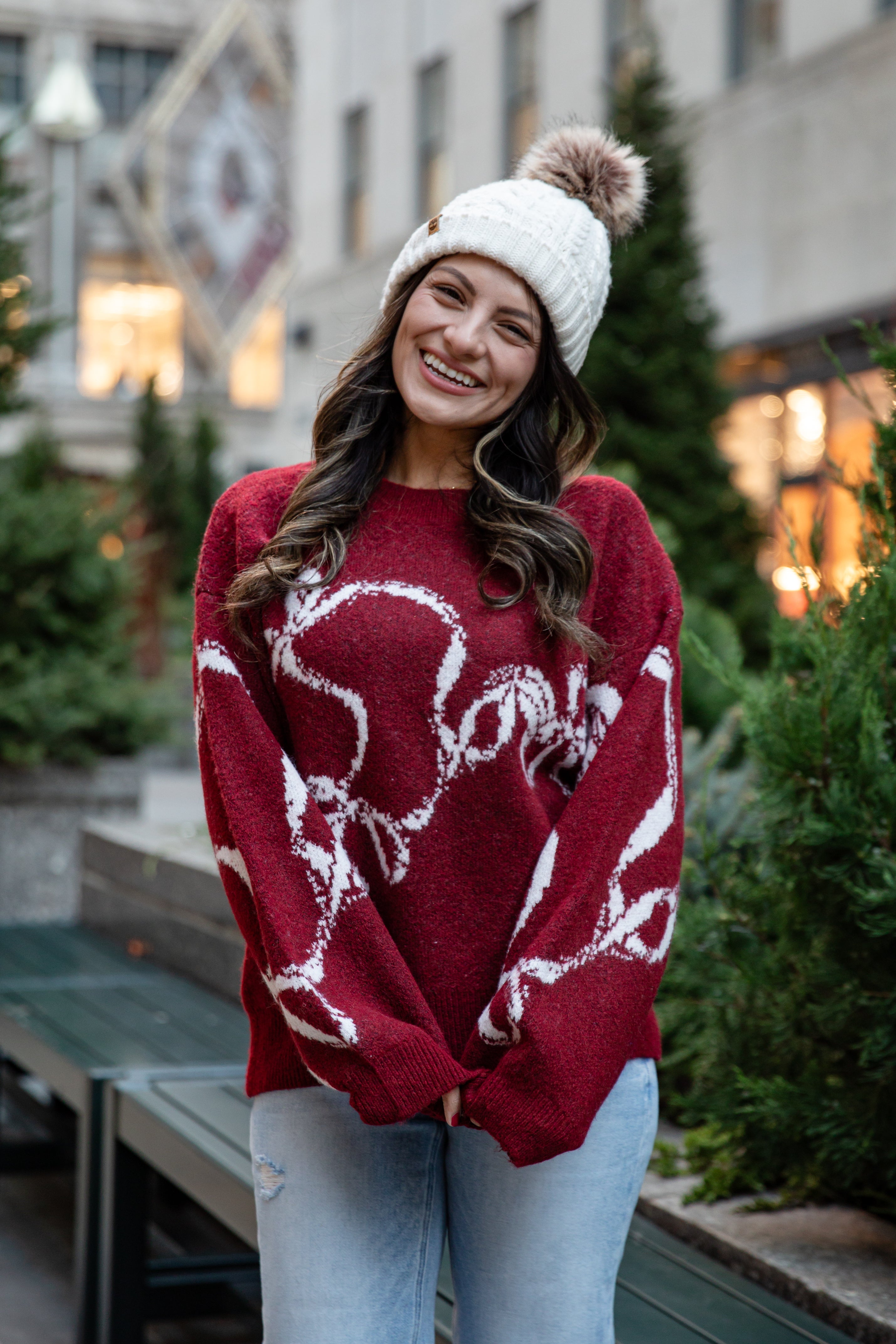 Woman wearing a red sweater with white patterns and a white beanie outdoors.