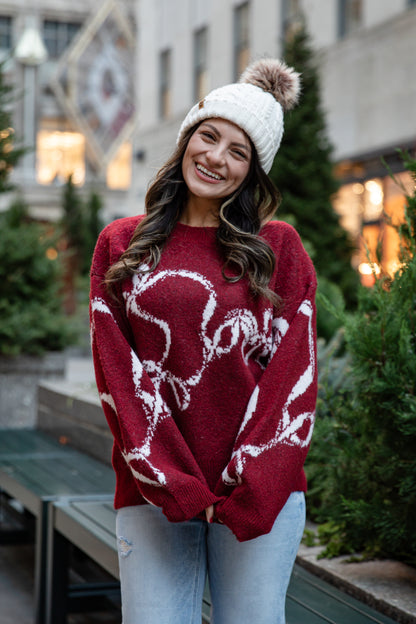 Woman wearing a red sweater with white patterns and a white beanie outdoors.