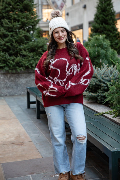 Woman wearing a red sweater with white patterns, light blue jeans, and a white knit hat outdoors.