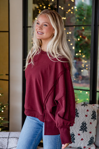 Woman wearing a maroon sweatshirt and blue jeans standing in front of a decorated window with lights.
