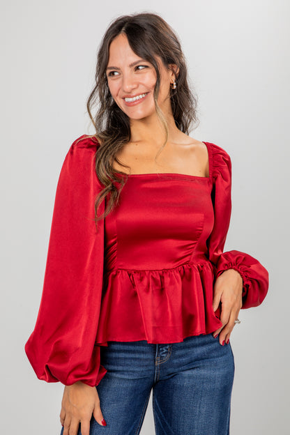 Woman wearing a red blouse with puffed sleeves against a gray background