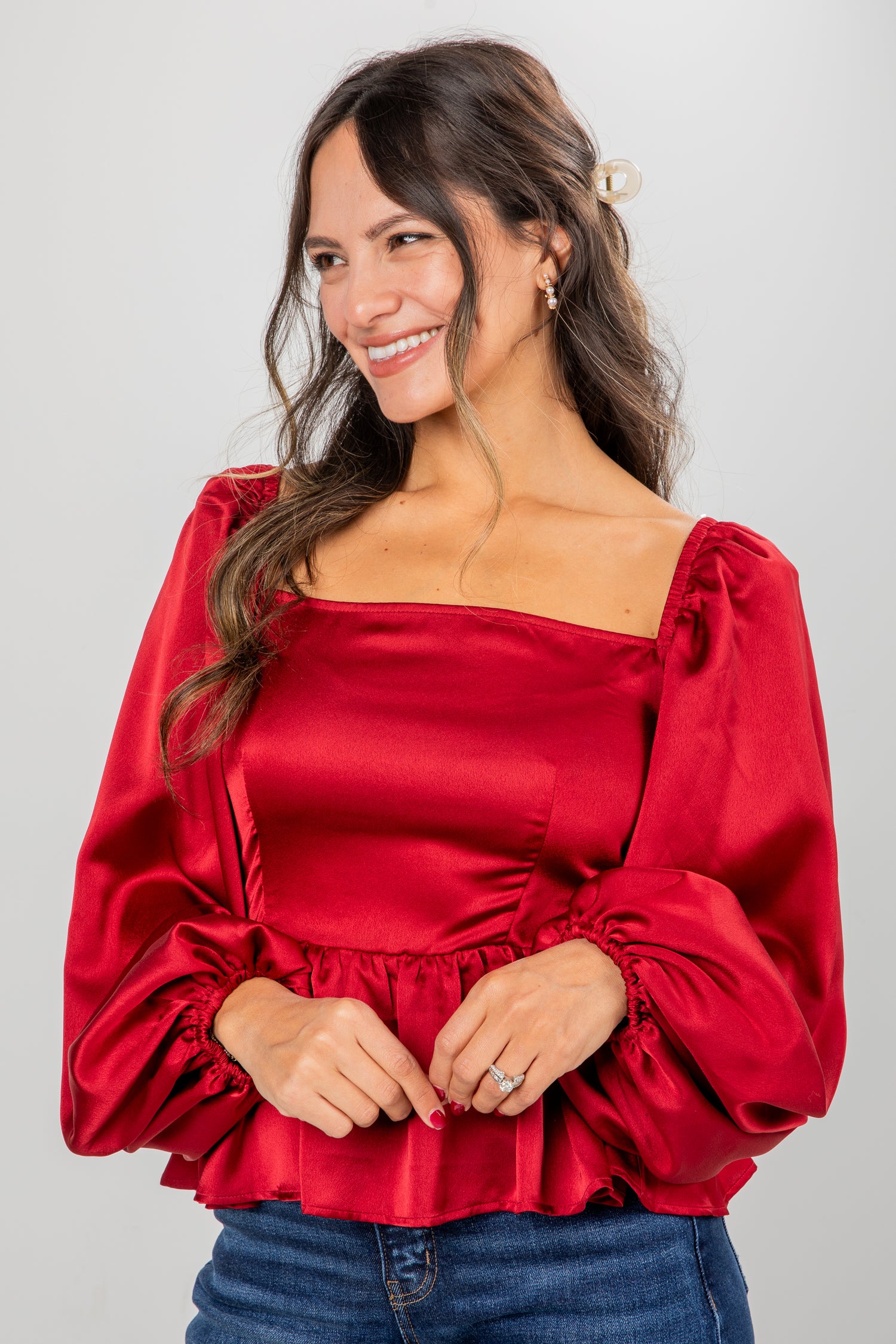 Woman wearing a red satin blouse with puffed sleeves against a gray background