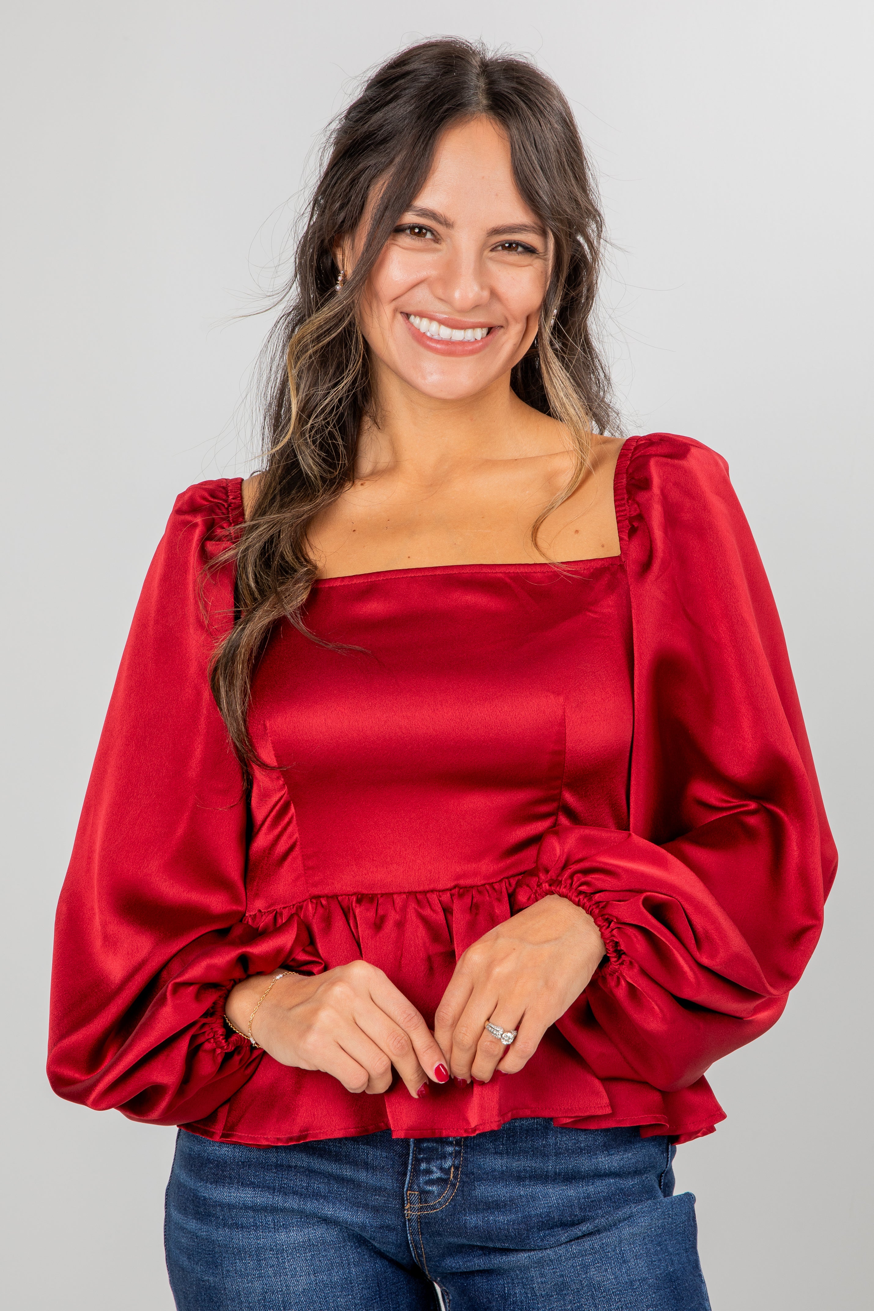 Woman wearing a red blouse with puffed sleeves on a gray background