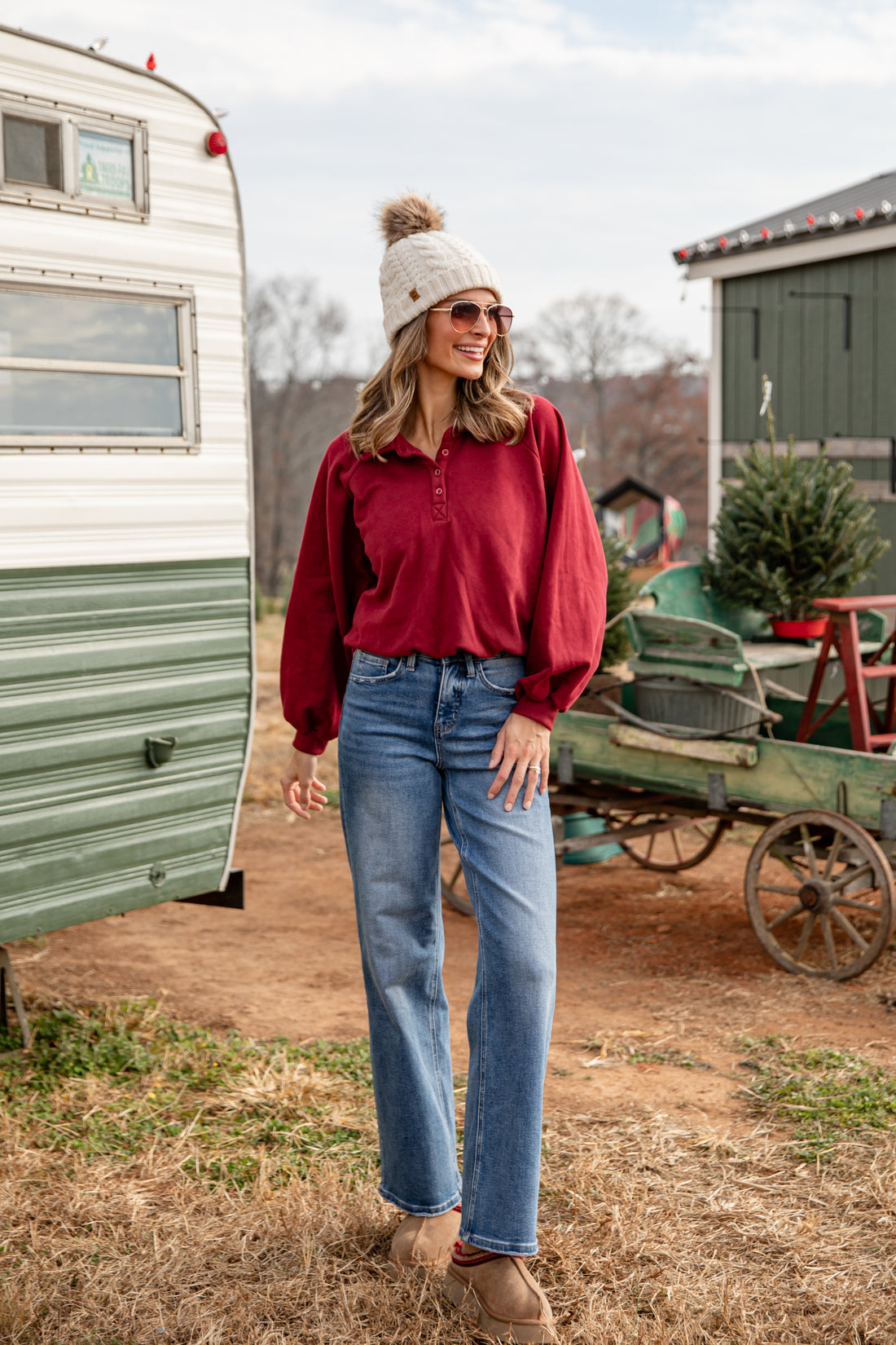 Woman in red shirt and blue jeans standing in front of a vintage trailer and green wagon.